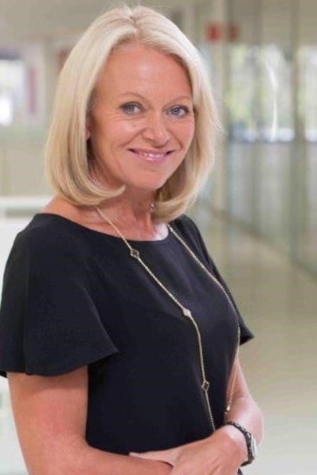 Alison Sharman wearing a black dress and standing, smiling