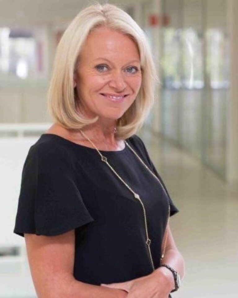 Alison Sharman wearing a black dress and standing, smiling